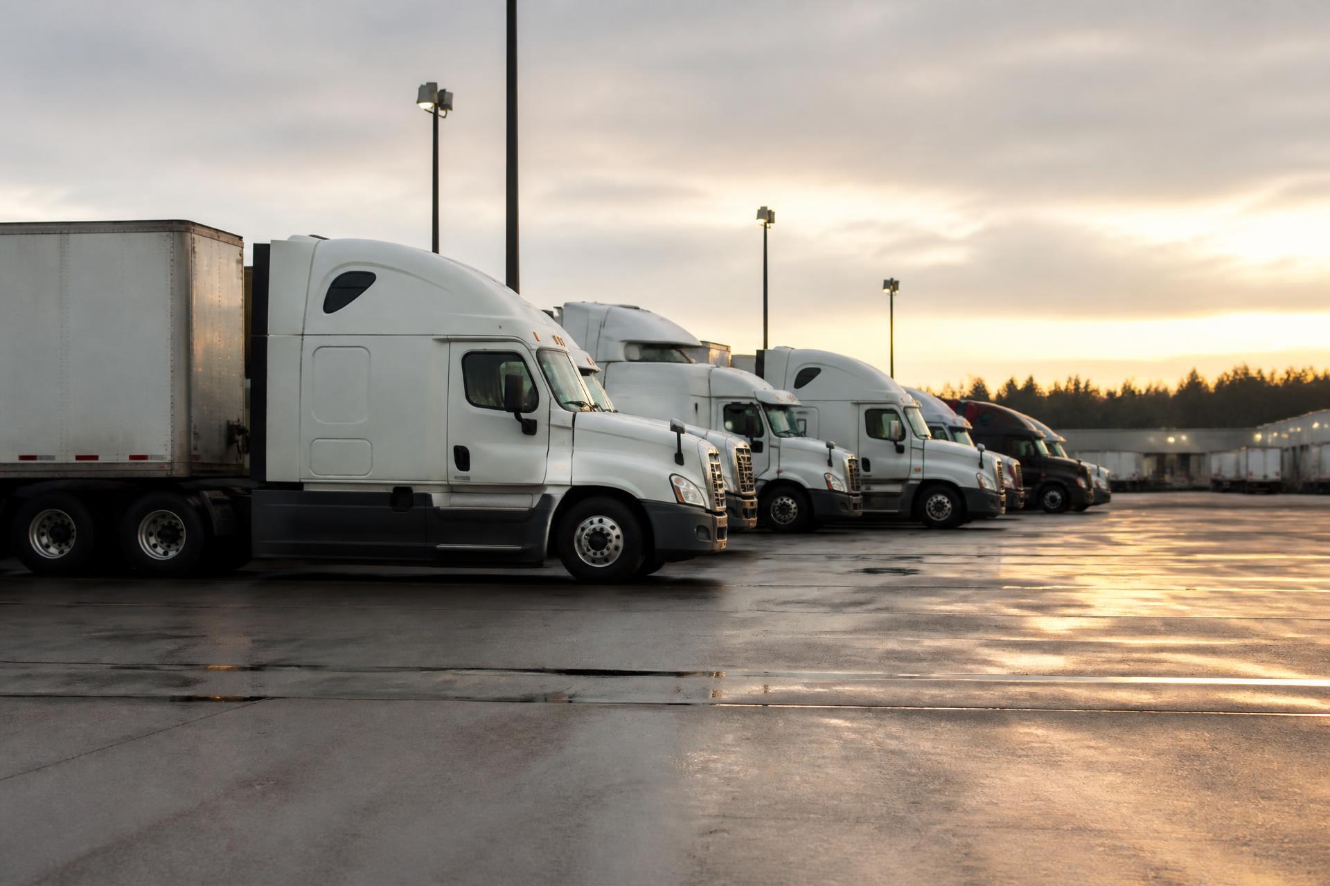 Row of commercial semi trucks and trailers parked at a logistics terminal at dawn